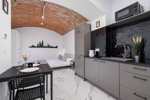 Cocina compacta con microondas, lavamanos y muebles de cocina modernos. En el fondo, se ve una cama con un mural de paisaje urbano.