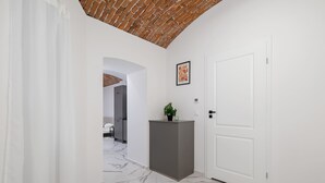 Ein Flur mit einer weißen Tür, einem grauen Podest mit einer Pflanze und einem gerahmten Bild an der Wand.
