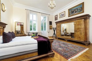 Un dormitorio amplio con una cama grande, un armario de madera, una araña y un ventanal con cortinas.