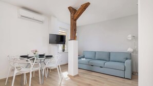 Een moderne zithoek met een lichtblauwe bank, een eettafel met witte stoelen en een houten decoratief element boven de bank.