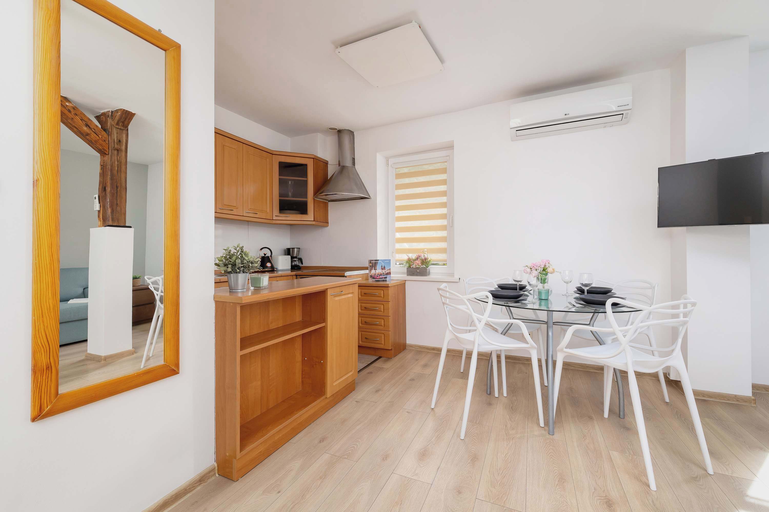 A modern kitchen with wooden cabinets, a dining table with white chairs, and a large mirror.