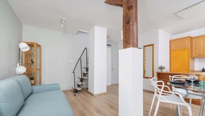 Een moderne woonkamer met een bank, een eettafel met stoelen, een trap en houten kasten.