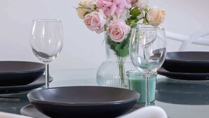 Een eettafel met zwarte borden, twee heldere wijnglazen en een vaas met roze en witte bloemen.