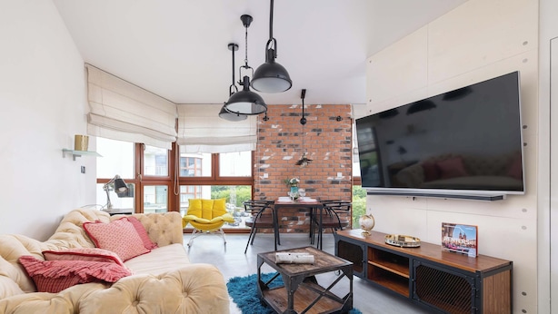 A modern living room with a sofa, coffee table, and TV. There is a brick wall and large windows.