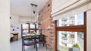 A dining area with a brick wall, a window with a view of buildings, and a table with chairs.