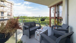 A balcony with wicker furniture, a potted plant, and a view of greenery and buildings.