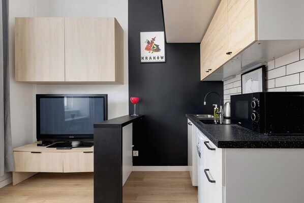 A modern kitchen with a black countertop, wooden cabinets, a black wall with a framed picture, and a television on a wooden stand.