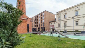 A playground with slides and swings, a brick building, and a beige building with windows.