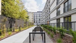 A modern building with a pathway lined with benches and small plants.