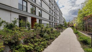 A modern building with a long, straight pathway flanked by greenery and a small seating area.