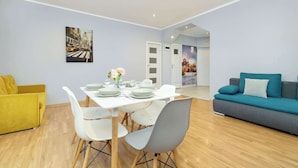 A modern living room with a dining area, featuring a sofa, a dining table set with plates and glasses, and a painting on the wall. - Bright Apartment in Krakow | Close to Market Square, Place to Work (Kraków)