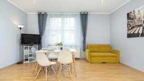 A modern living room with a dining area, a sofa, a flat-screen TV, and a window with curtains. - Bright Apartment in Krakow | Close to Market Square, Place to Work (Kraków)