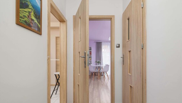 Un pasillo con puertas de madera que dan a un comedor con mesa y sillas.