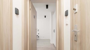 Un couloir avec des portes en bois, un interrupteur et un clavier de sécurité fixé au mur.