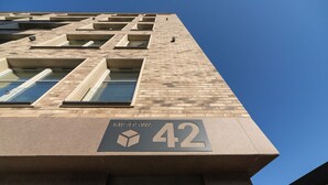 Un bâtiment se dressant sous un ciel dégagé, dont la façade présente un grand chiffre « 42 » et le mot « MICDGWA ».