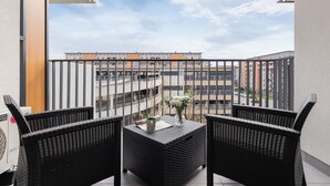 Un balcón con dos sillones de mimbre, una mesa y un jarrón con flores.