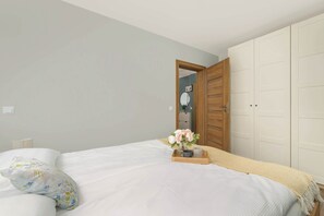 A bedroom with a bed, a bedside table with a vase of flowers, and a wardrobe.