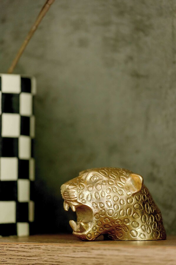 A golden leopard figurine on a wooden surface with a checkered vase in the background.