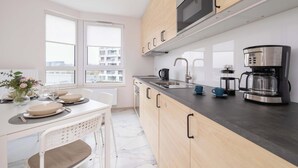 A modern kitchen with wooden cabinets, a stainless steel microwave, a coffee maker, and a dining area with a table set for two. - Elegant Apartment with Balcony | Parking | Workspace (Kraków)