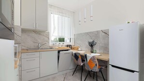 A modern kitchen with marble countertops, white cabinetry, a built-in dishwasher, and a white refrigerator.