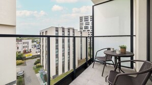 A balcony with a view of a cityscape, featuring a table with chairs and a potted plant.