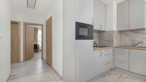 A modern kitchen with white cabinets, a black microwave, marble countertops, and a wooden door.