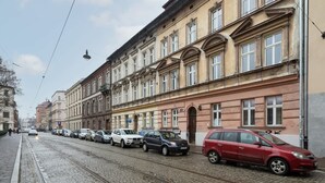 Calle con tranvías, coches estacionados y una hilera de edificios históricos con ventanas de arco y estilo arquitectónico clásico.