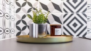Una planta en maceta con flores sobre una bandeja, un tarro etiquetado como “RELAXING SCENT” y un florero metálico.