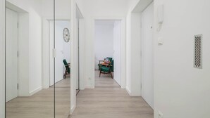 Un pasillo con un separador de vidrio, piso de madera y un comedor con sillas verdes y una mesa al fondo.