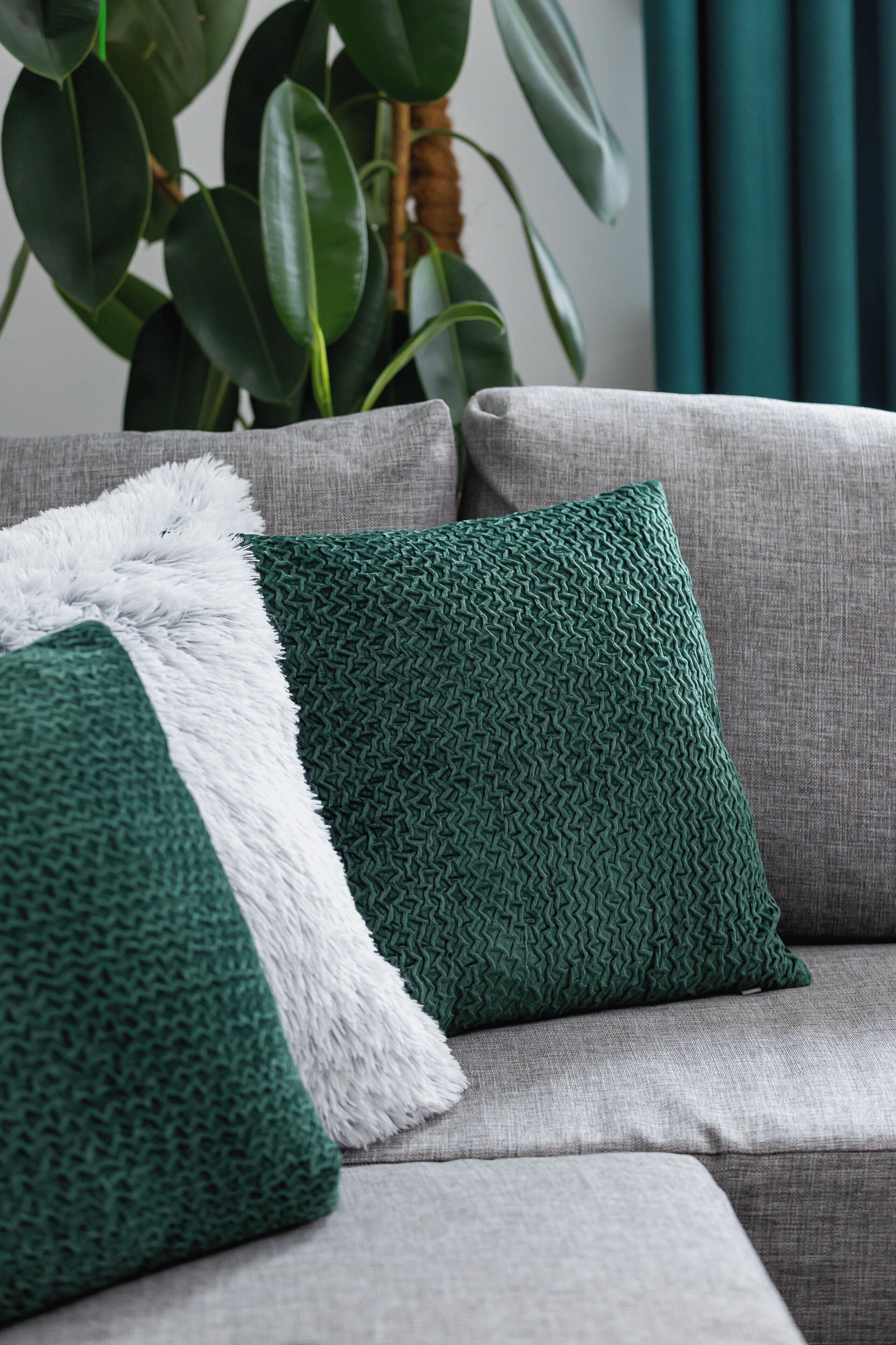 Ein graues Sofa mit einem grün gemusterten Kissen und einer weißen, flauschigen Decke.