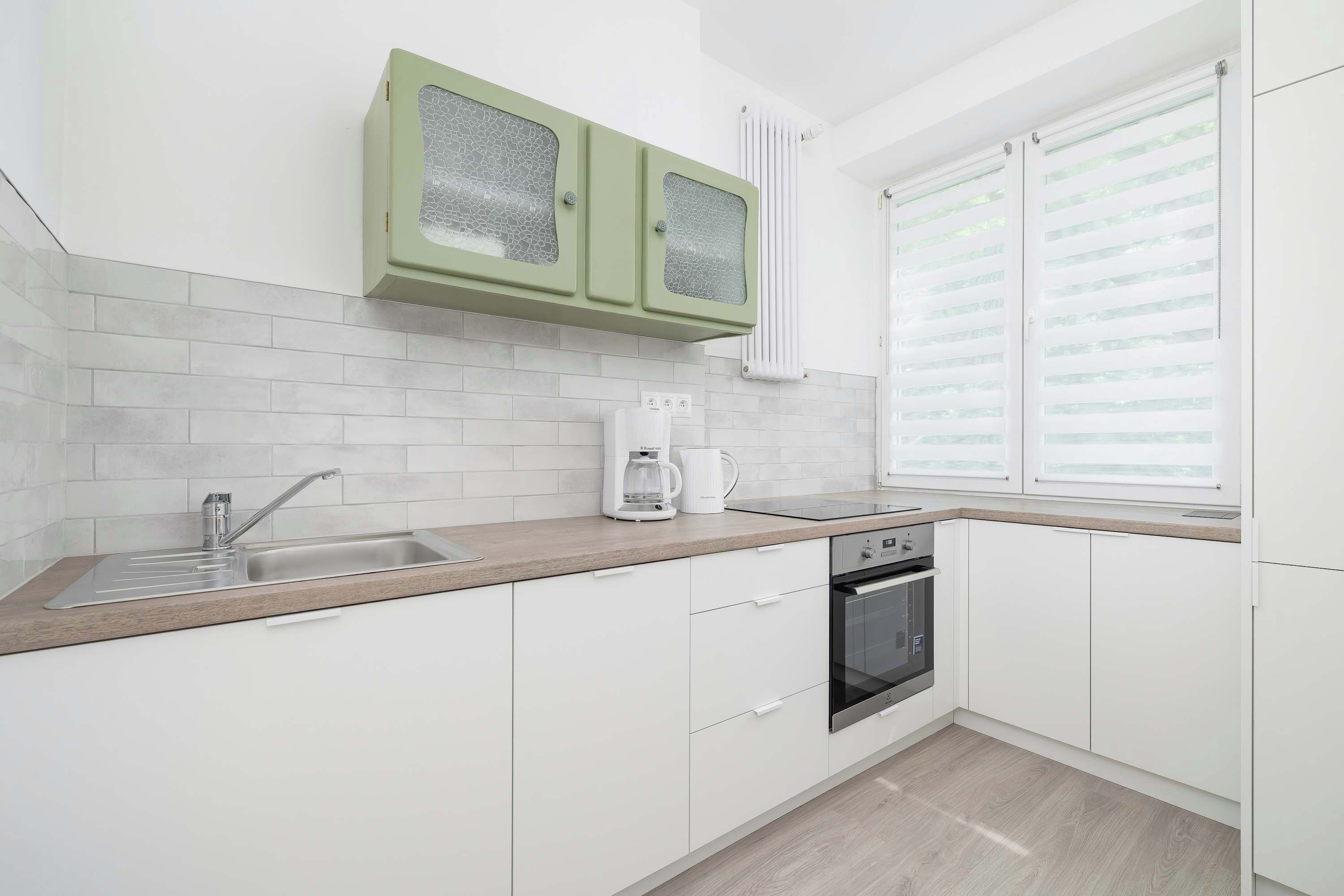 Una cocina moderna con armarios blancos, un lavamanos de acero inoxidable, una cafetera y un horno empotrado.