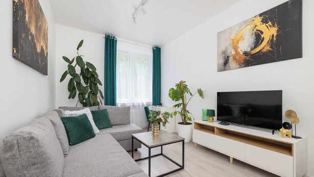 Una sala de estar moderna con un sofá gris, una mesa de centro, un televisor sobre un mueble blanco y dos grandes cuadros abstractos.