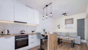 Una cocina moderna con armarios blancos, horno empotrado y un comedor con mesa de madera y taburetes de bar.