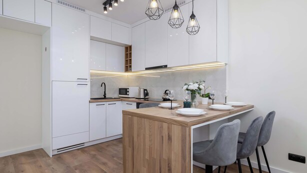 Una cocina moderna con armarios blancos, una isla de madera y una zona de comedor con sillas grises.