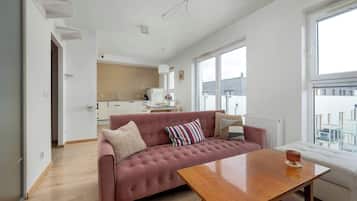 A modern living room with a sofa, a wooden coffee table, and a view of the city through large windows.