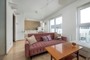 Un salon moderne avec un canapé, une table basse en bois et une vue sur la ville grâce à de grandes fenêtres.