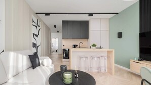Una sala de estar moderna con un sofá, una mesa redonda con una vela y una cocina con barra.