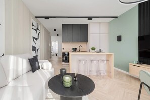 A modern living room with a sofa, a round table with a candle, and a kitchen area with a bar.