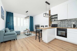 A modern kitchen with white cabinets, a wooden countertop, and a built-in oven. There is a grey sofa and a small table with a plant. - Stylish Apartment | Balcony | Close to Galeria Bonarka (Kraków)