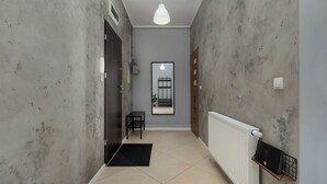 Een gang met een radiator, een zwarte tafel met een stoel, een hanglamp en een spiegel aan de muur.