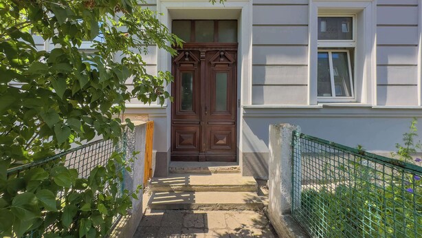Een huis met een dubbele houten deur, een klein raam en een betonnen trap die naar de ingang leidt.