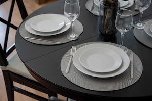 A round dining table with a black tablecloth, white plates, cutlery, and empty wine glasses.