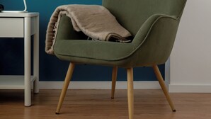 Een groene fauteuil met een plaid, een witte bijzettafel met een laptop, en een wand in teal.