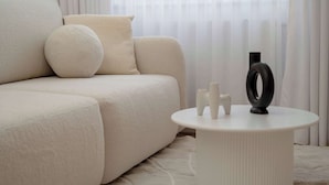Ein stilvolles Wohnzimmer mit einem beigefarbenen Sofa, einem runden Hocker und einem weißen Beistelltisch mit Dekoration.