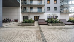 Ein modernes Gebäude mit mehreren Balkonen, einem gepflasterten Innenhof und einigen Fahrrädern vor der Tür.