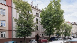 Una hilera de edificios residenciales de varios pisos, autos estacionados y árboles en la fachada.