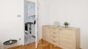Una cocina moderna con armarios blancos, un mueble de madera con cajones, una pequeña mesa redonda con una planta y una maceta encima del mueble.