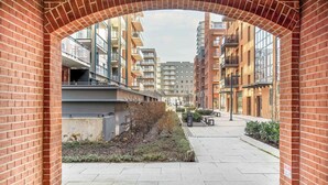 A brick archway framing a pathway leading to a row of modern apartment buildings with balconies.