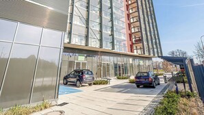 A modern high-rise building with a glass facade, a parking area with cars, and a bench in the foreground.