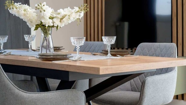 Un comedor moderno con una mesa de madera, sillas tapizadas de gris y un jarrón con flores blancas.